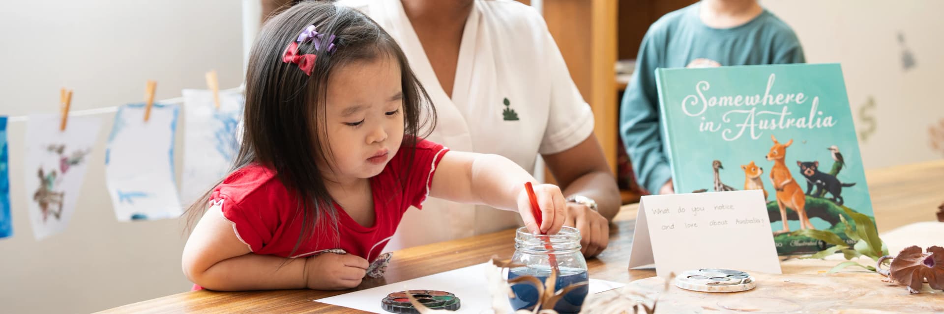 Child painting with watercolours beside an educator at a Simba Education Sydney early learning centre